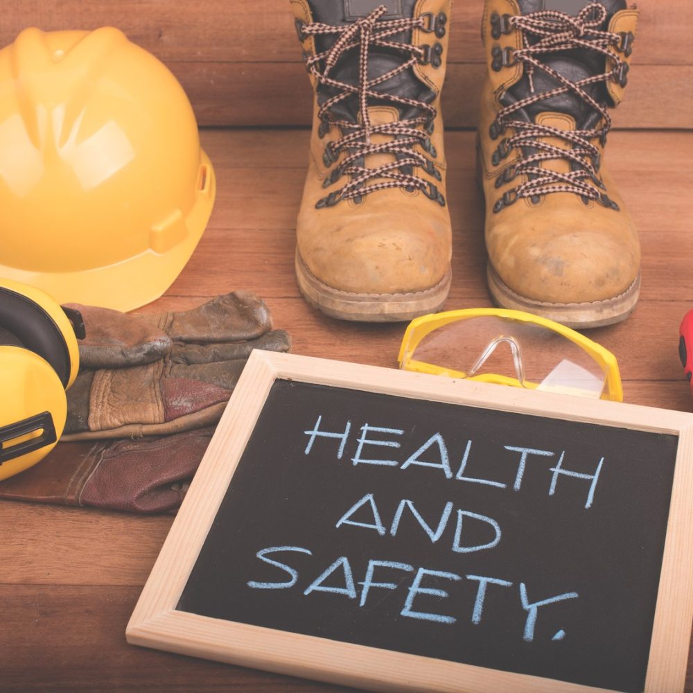 Standard construction safety equipment on wood background with health and safety text on blackboard.